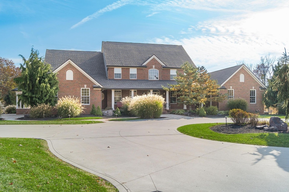 Front exterior of a brick home with a curved driveway and landscaped yard.