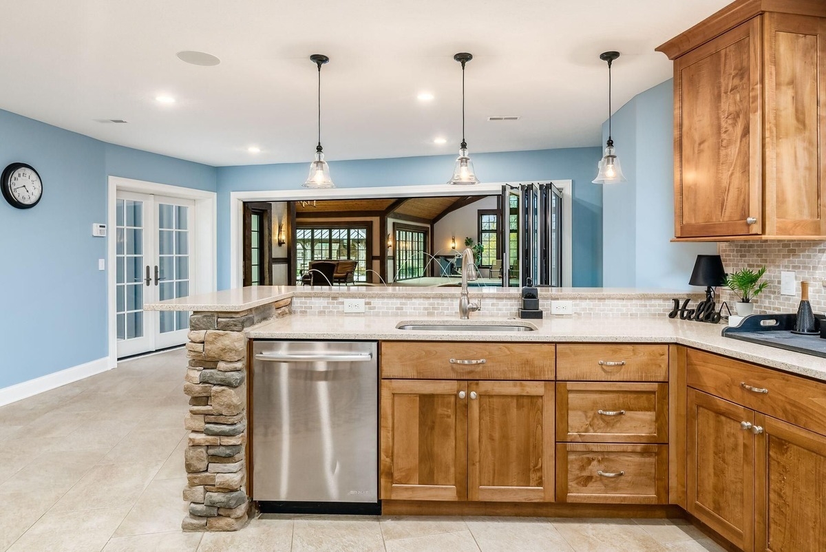 A kitchenette with wood cabinets, pendant lighting, and a view of the pool area.