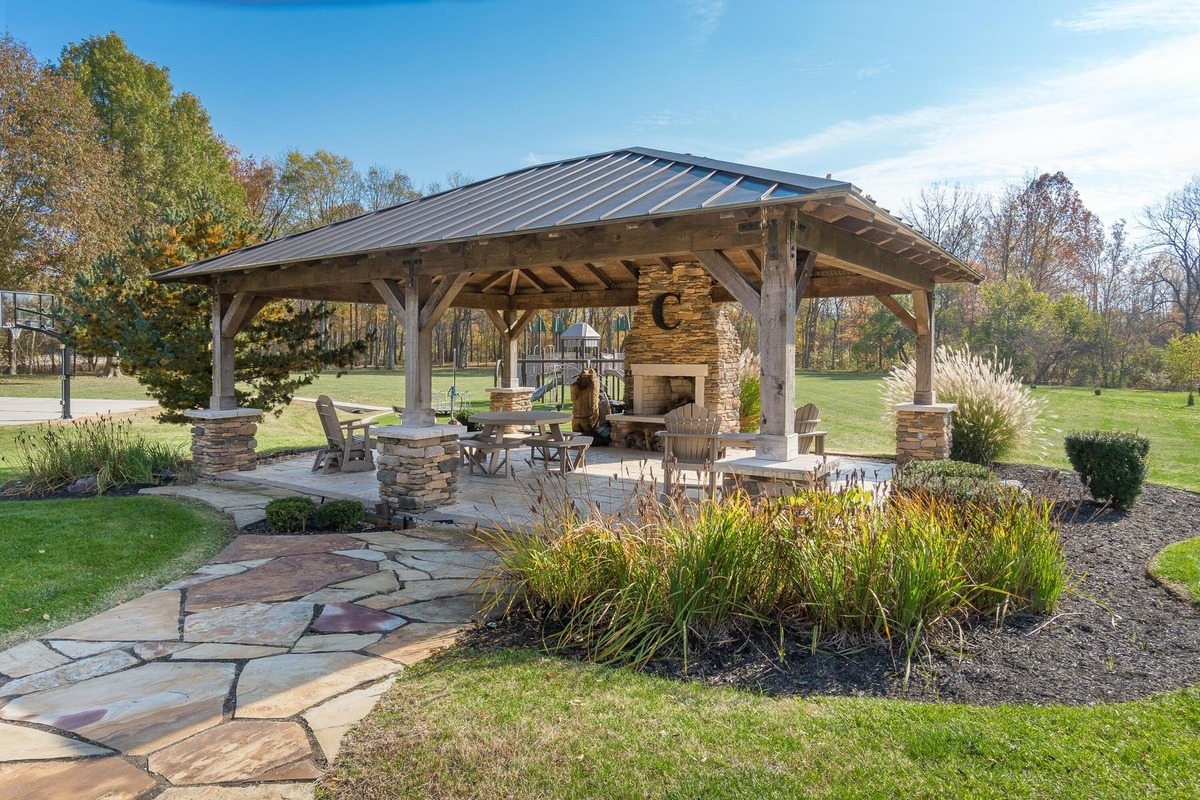 utdoor pavilion with stone accents, a fireplace, and seating area surrounded by gardens.