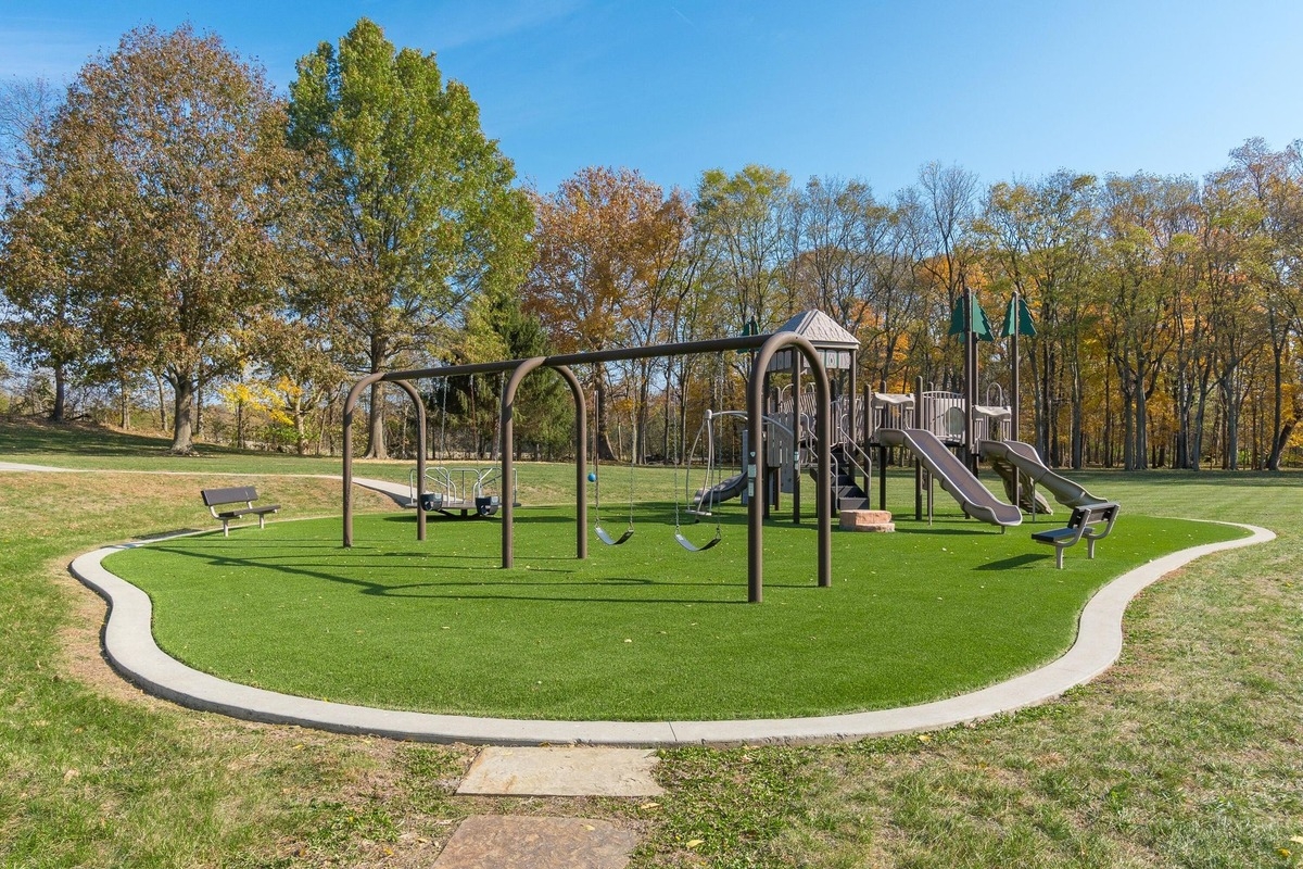 Playground with slides, swings, and benches on a landscaped lawn.