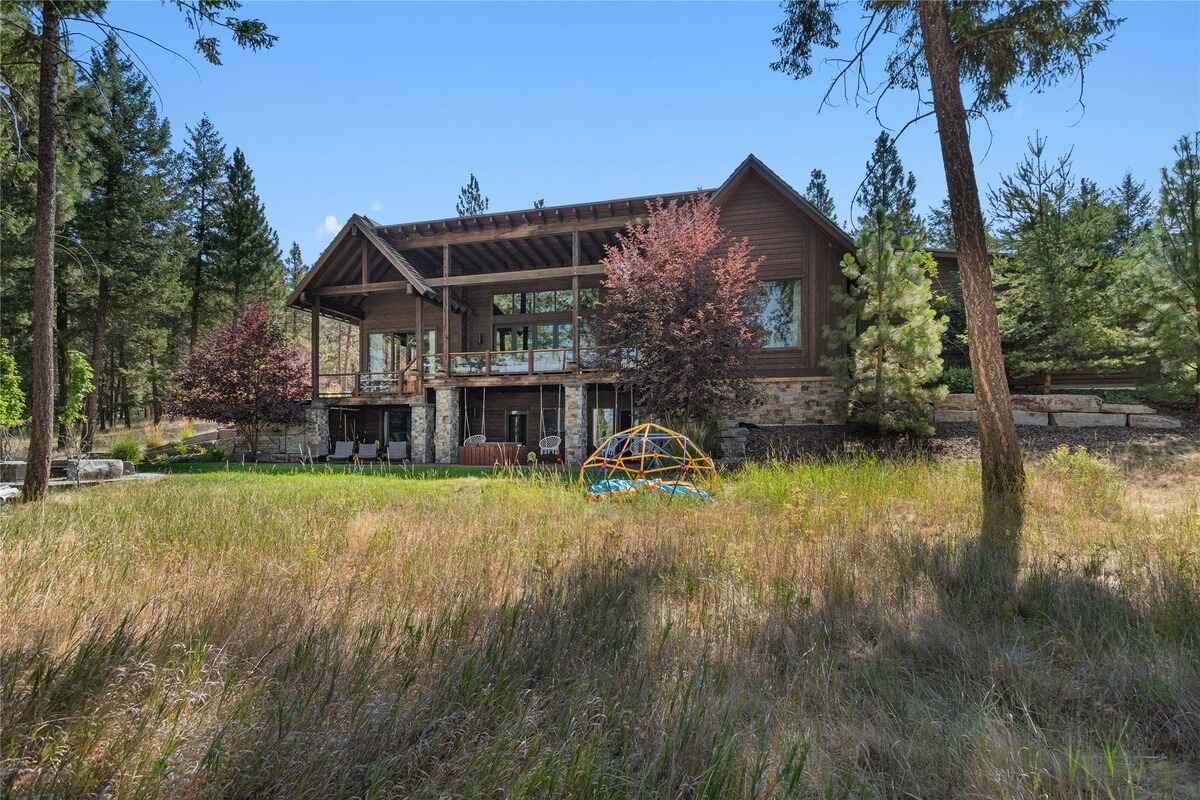 Rustic home surrounded by trees features a spacious wooden deck and stone accents, blending seamlessly into the natural landscape.