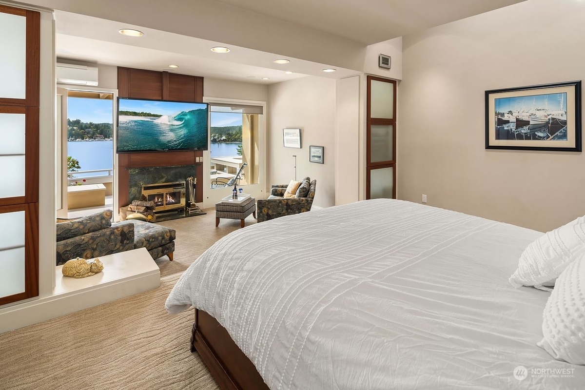 Master bedroom with king-size bed, fireplace, and large windows offering a water view. 