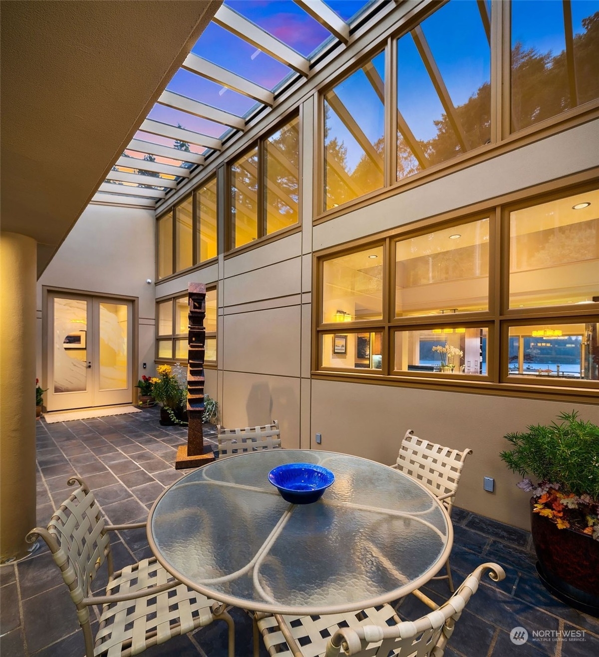 Covered patio with glass-top table and chairs, surrounded by large windows and skylights.