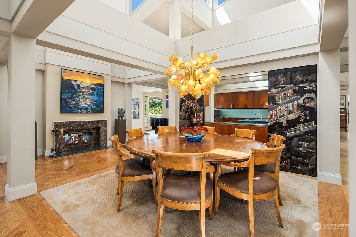 Large dining room with hardwood floors, a large round table, and artwork features a high ceiling with skylights.