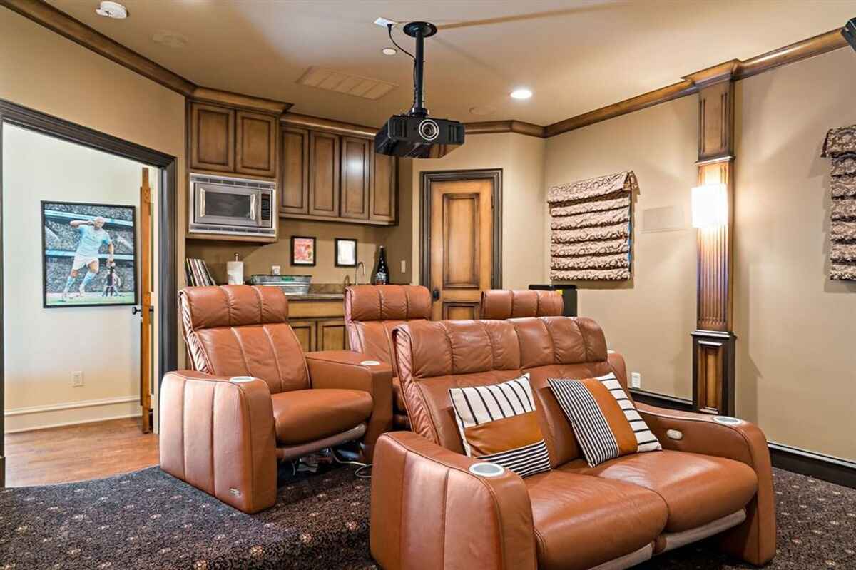 Private theater room with recliner seating, a projector, and warm lighting.