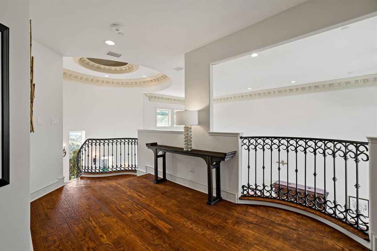 A bright hallway with wood flooring and decorative wrought-iron railings overlooking the space below.