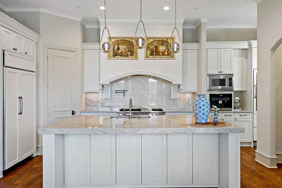 A bright kitchen with white cabinetry, marble countertops, and pendant lighting.