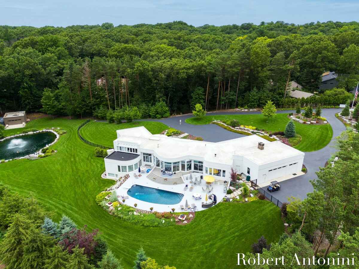 Large white house with a pool and landscaping sits on a large lot surrounded by trees.