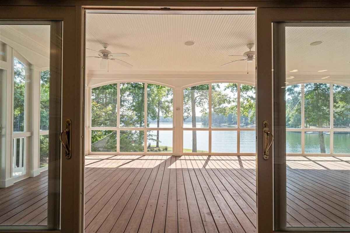 Large screened porch with wooden flooring and ceiling fans offers a view of the surrounding lake.