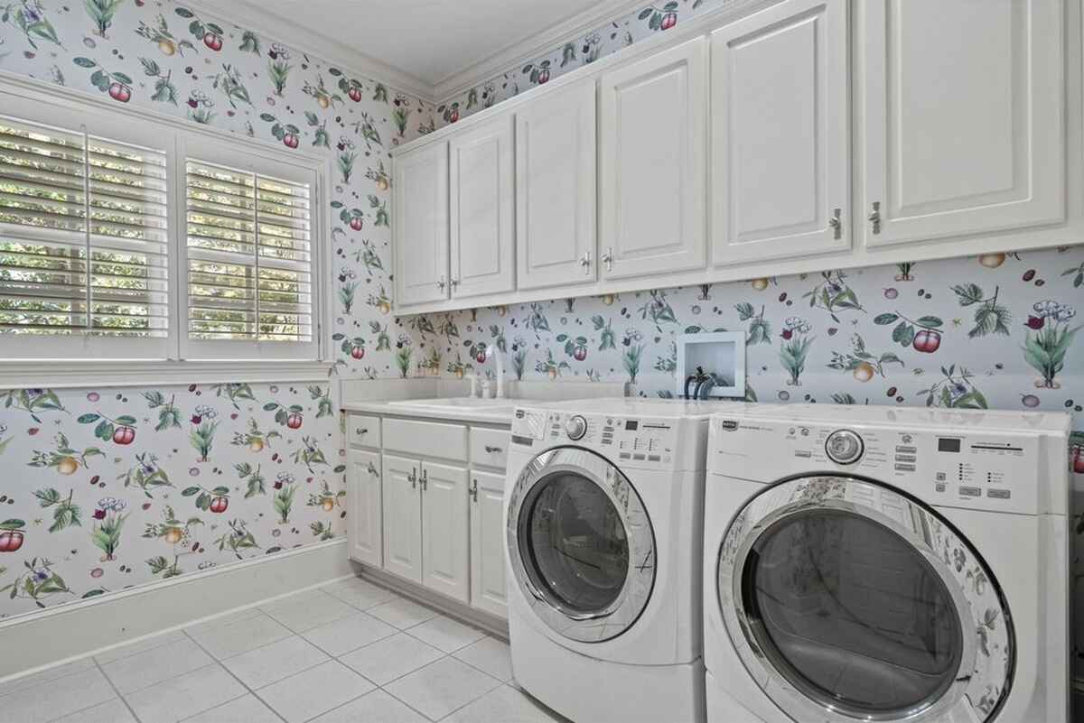 Laundry room features patterned wallpaper, cabinetry for storage, and a modern washer and dryer setup.