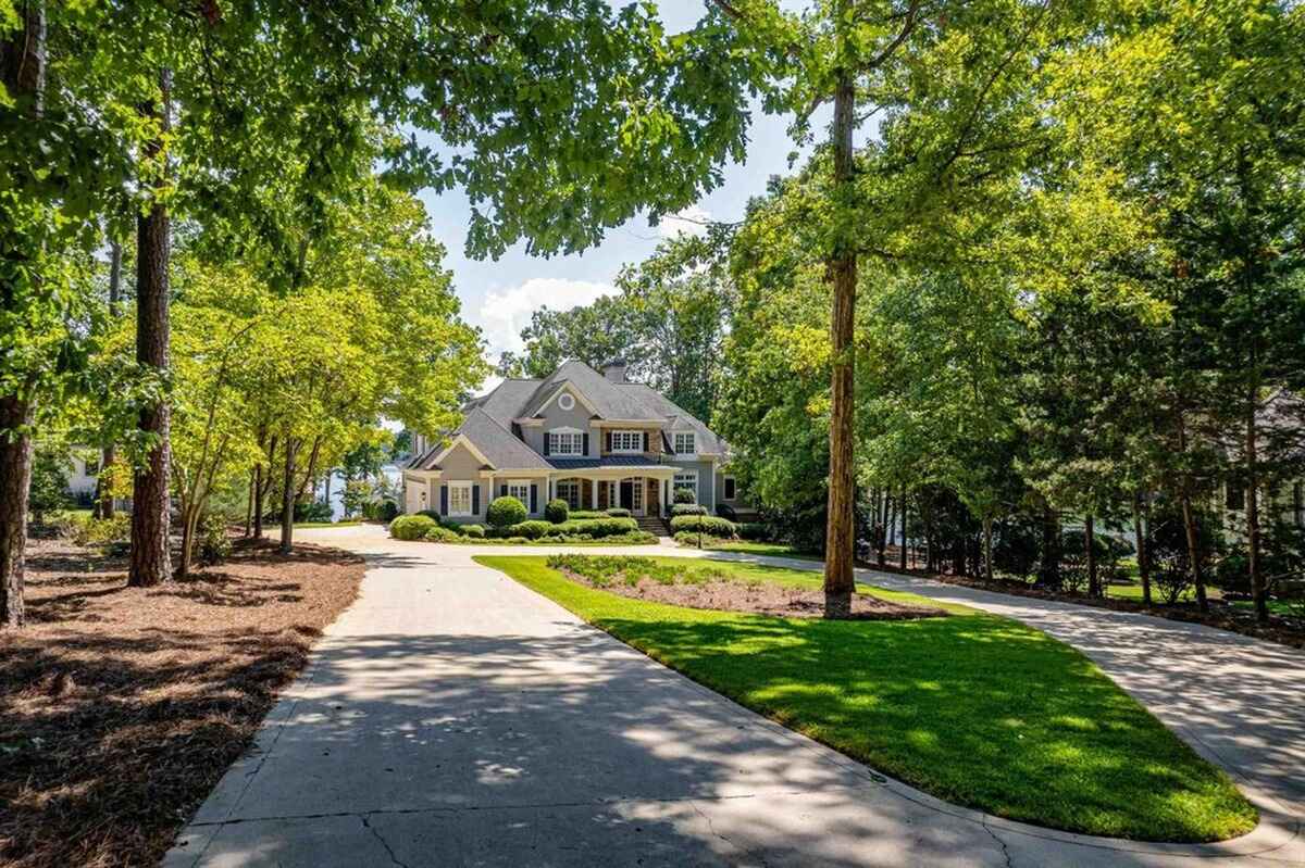 Long driveway surrounded by trees leading to a grand home with a lake view.