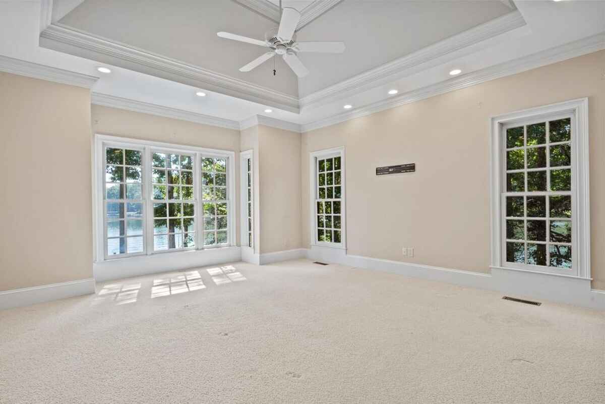 Bedroom with large windows, tray ceiling, and neutral carpeting creates a serene space with water views.