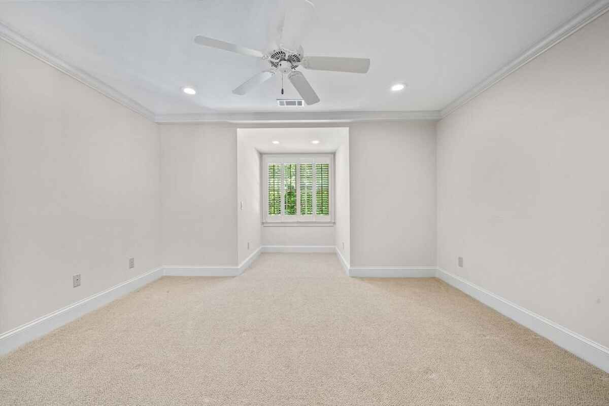 A carpeted bedroom is shown, featuring white walls, white baseboards, and a ceiling fan.