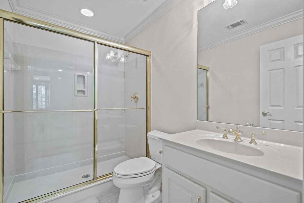 White cabinets, a shower with glass doors and gold trim, and a toilet are in a small bathroom.