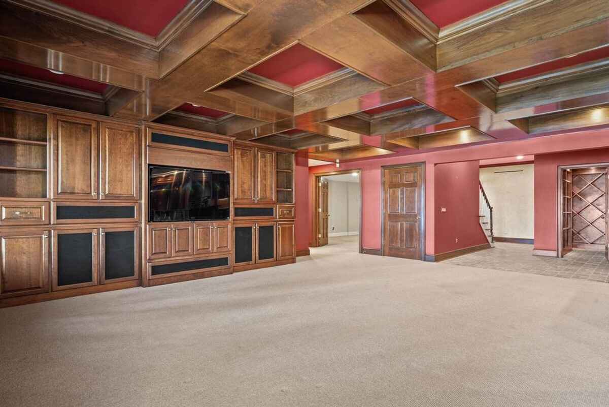 Spacious media room features a coffered wood ceiling, built-in cabinetry, and a wall-mounted TV.