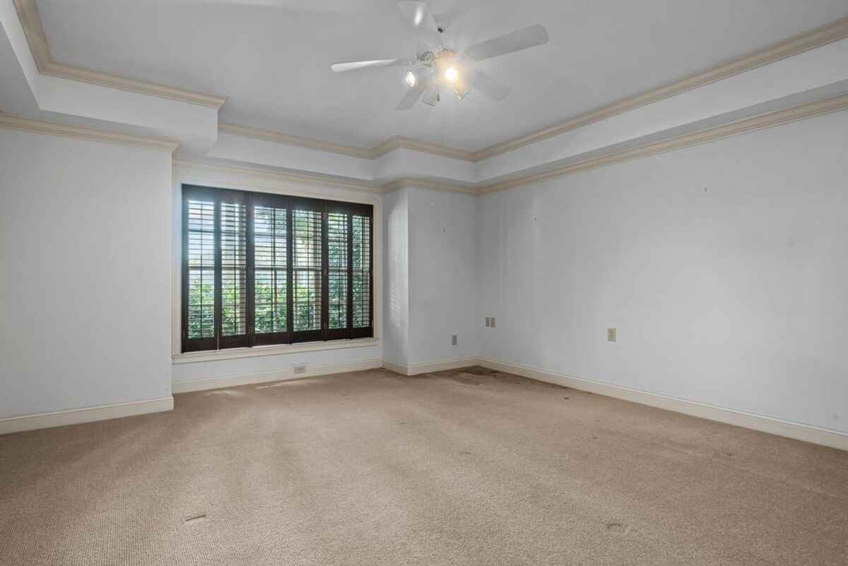 Bedroom displays large windows with dark wooden shutters and a tray ceiling.