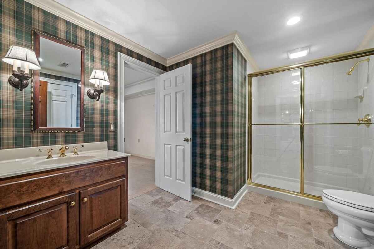 Bathroom presents plaid wallpaper, gold-framed shower, and a single vanity.