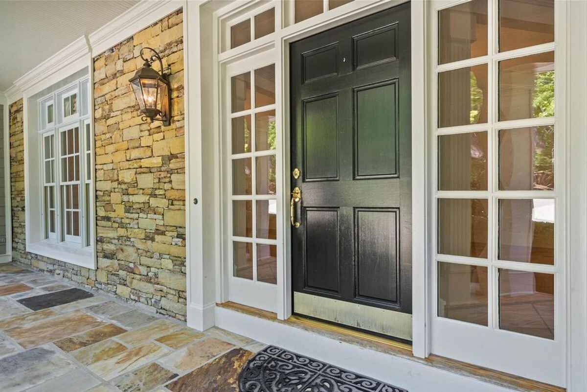 Black front door framed by glass panels and stone walls on a tiled porch.