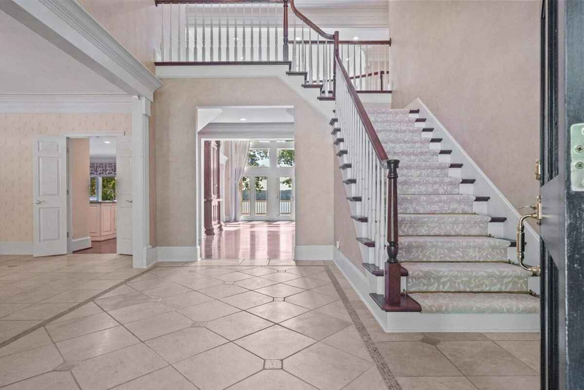 Spacious foyer with tiled flooring, a staircase, and a view of the lake through large windows.