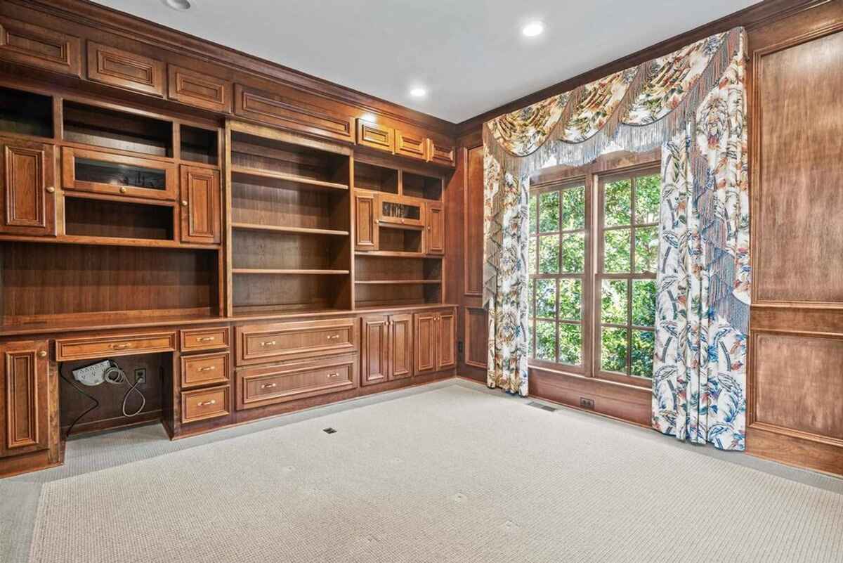 Wood-paneled study with built-in shelves, a desk, and large windows with ornate curtains.