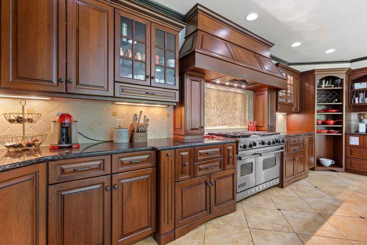 Large kitchen with dark wood cabinets, granite countertops, and stainless steel appliances.