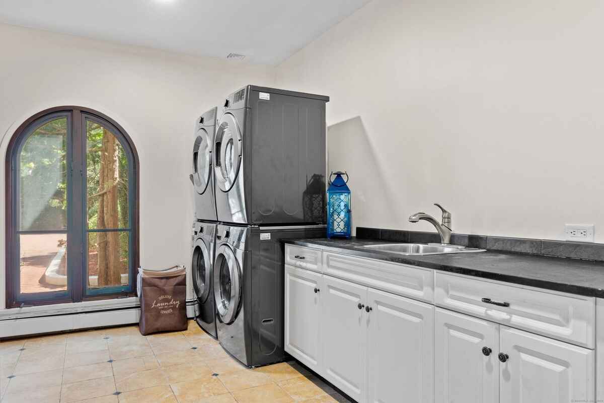 Laundry room with stacked washer and dryer, white cabinets, and arched window.