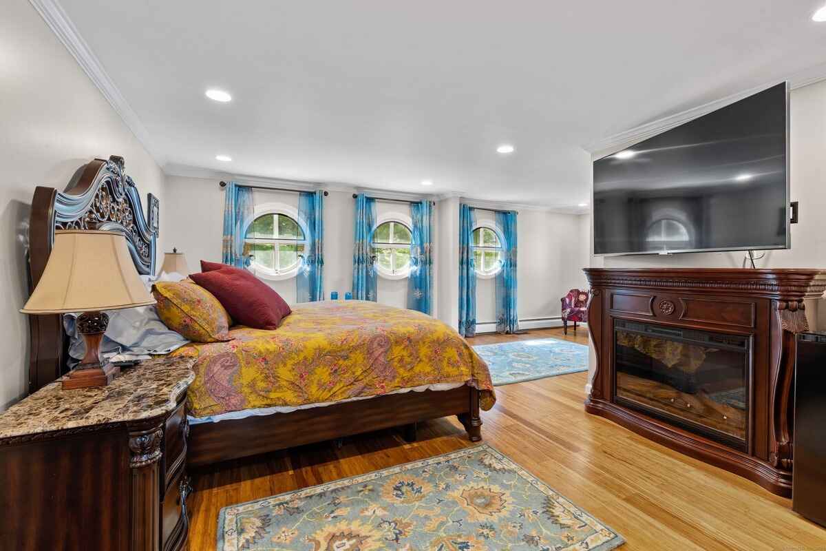 Bedroom with hardwood floors, circular windows, and a large flat-screen TV above a fireplace.