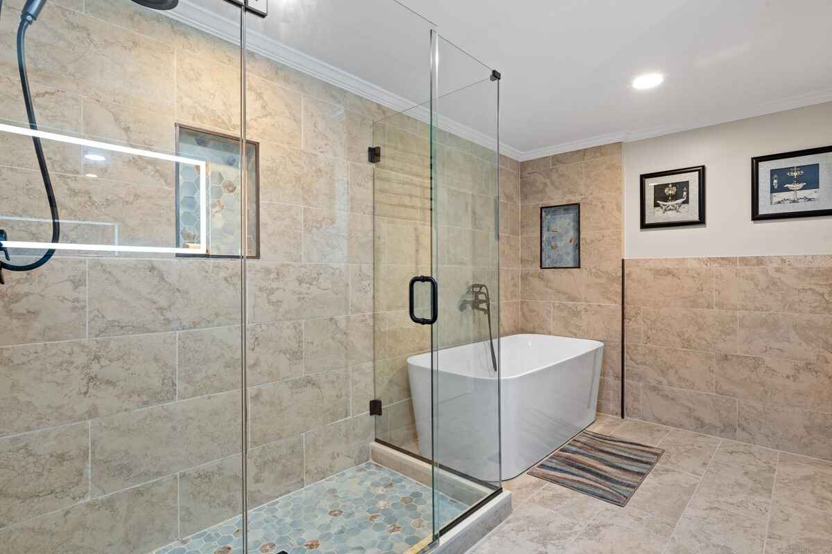 Bathroom with a glass shower enclosure, a freestanding bathtub, and beige tile.