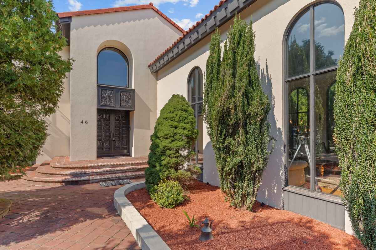 Landscaped area with red mulch and shrubs in front of a Mediterranean-style house.