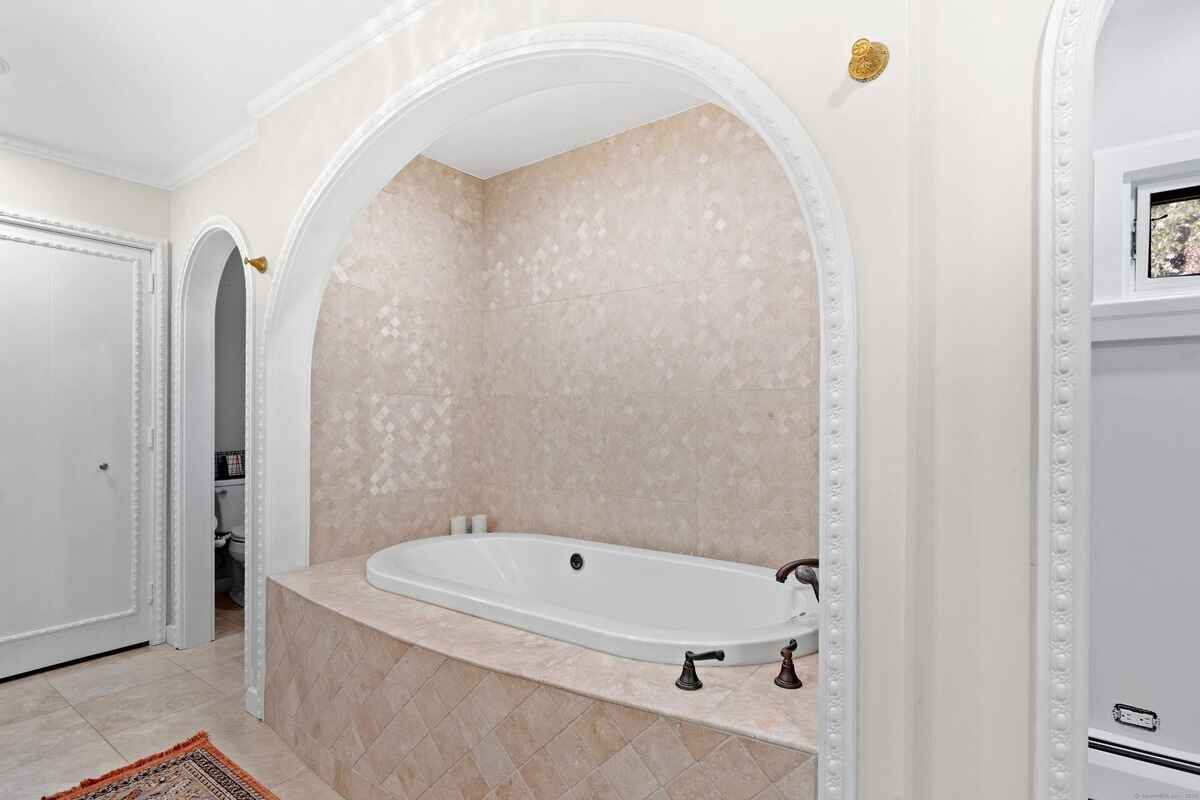 Bathroom with an arched alcove containing a freestanding bathtub and beige tile.