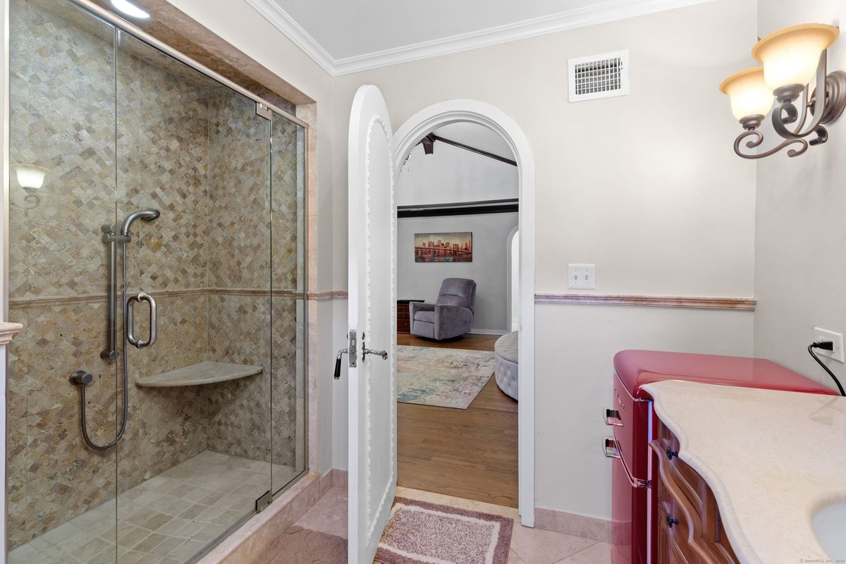 Bathroom with a glass shower, arched doorway to another room, and a red mini-refrigerator.