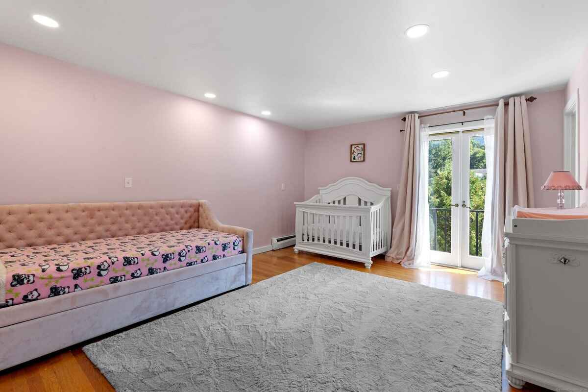 Nursery with pink walls, a daybed, a crib, and French doors leading to a balcony.