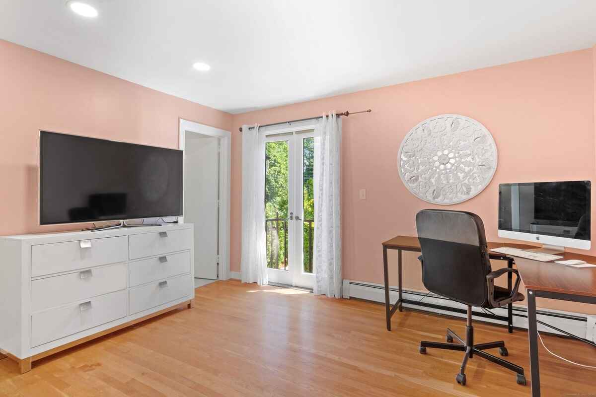 Room with peach walls, hardwood floors, a flat-screen TV, and a workspace with a computer.