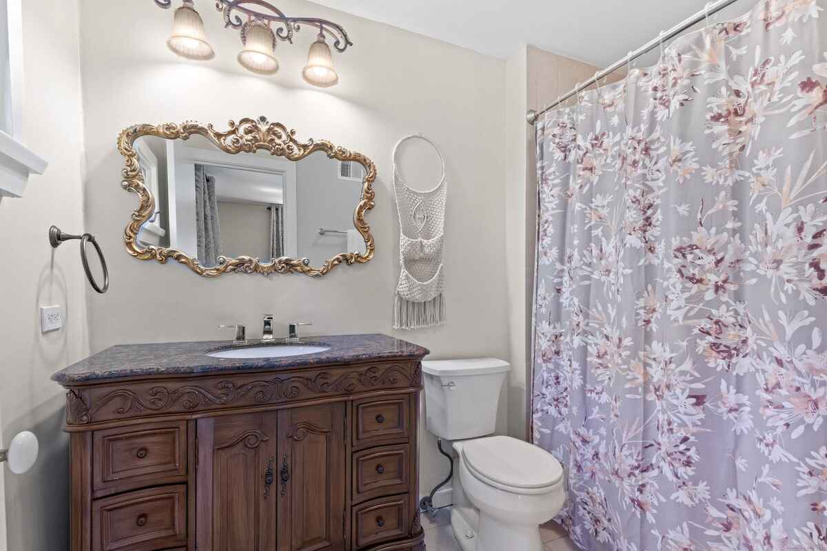 Bathroom with dark wood vanity, ornate mirror, and floral shower curtain.