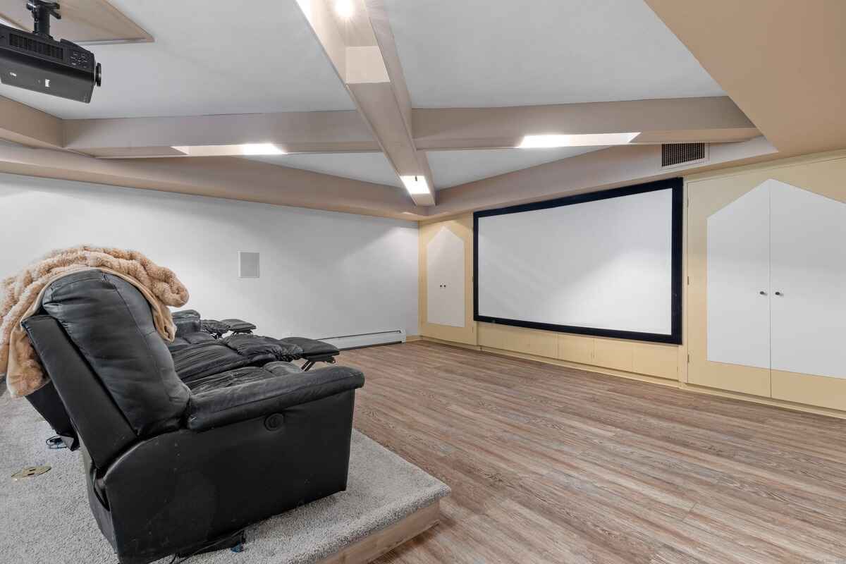 Home theater room with a large projection screen, black leather reclining seats, and wood flooring.