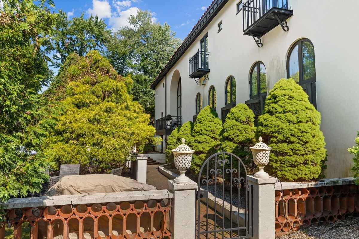 Backyard of a large house with a gated entrance, landscaping, and patio furniture.