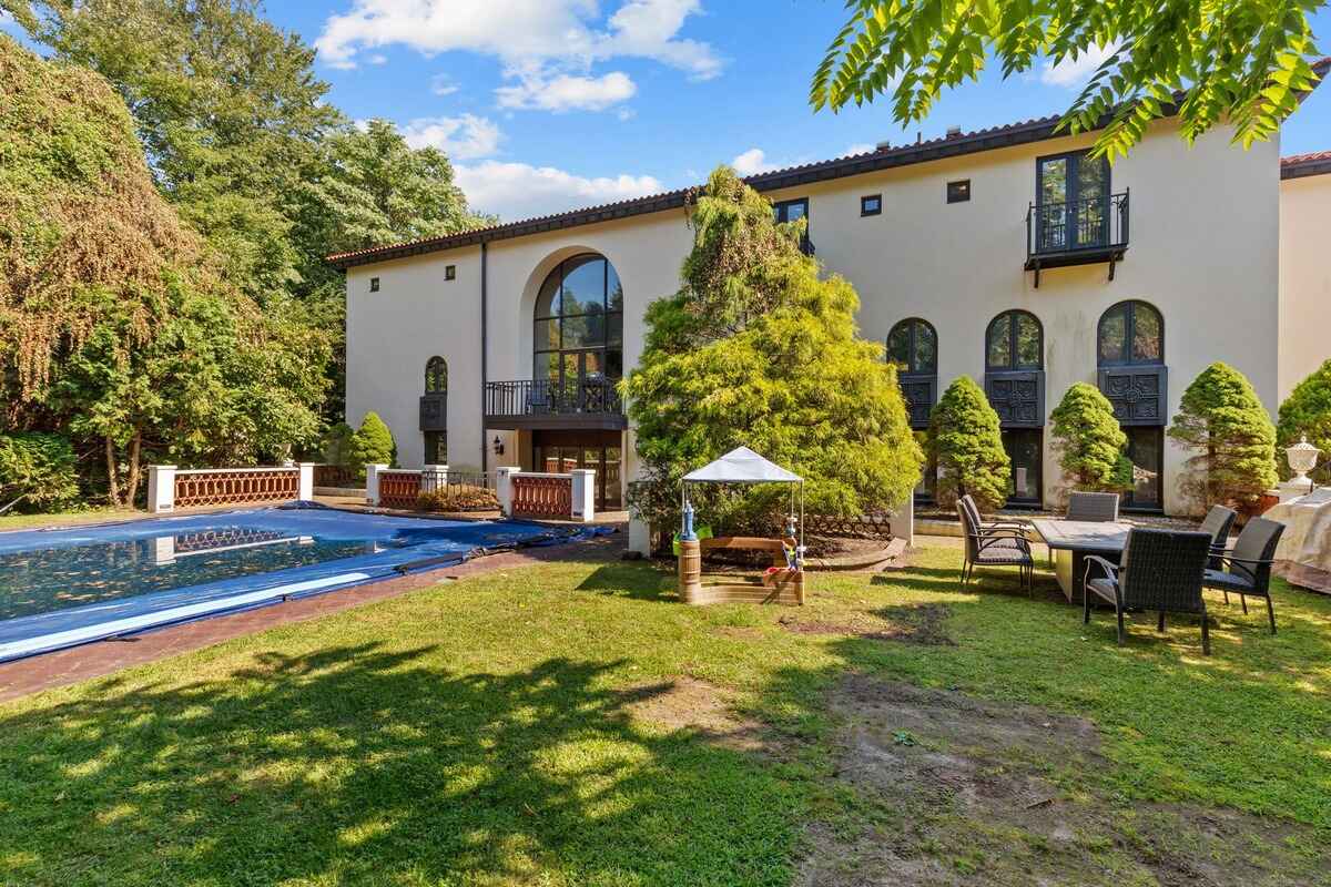 Large house with a swimming pool and patio furniture in a lush green backyard.