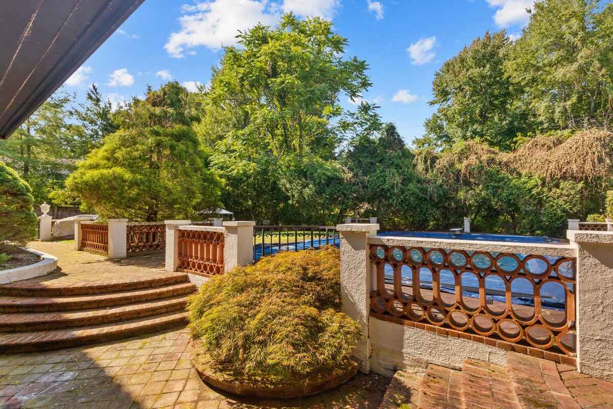 Brick patio with steps leading to a swimming pool, surrounded by landscaping and a decorative fence.