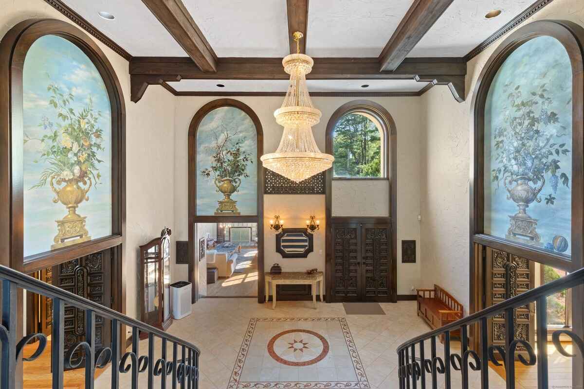 Large entryway with a grand chandelier, arched windows with painted murals, and ornate doors.