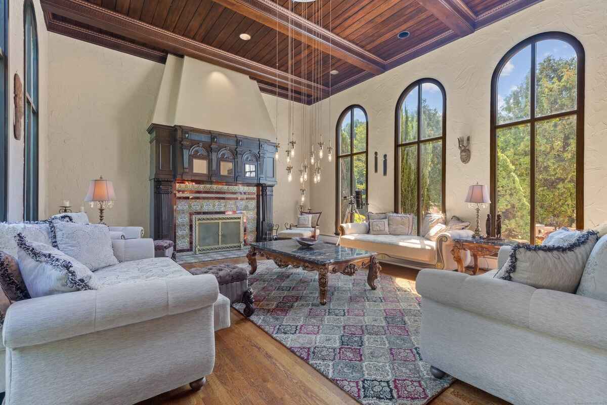 Living room with hardwood floors, arched windows, and a large ornate fireplace.