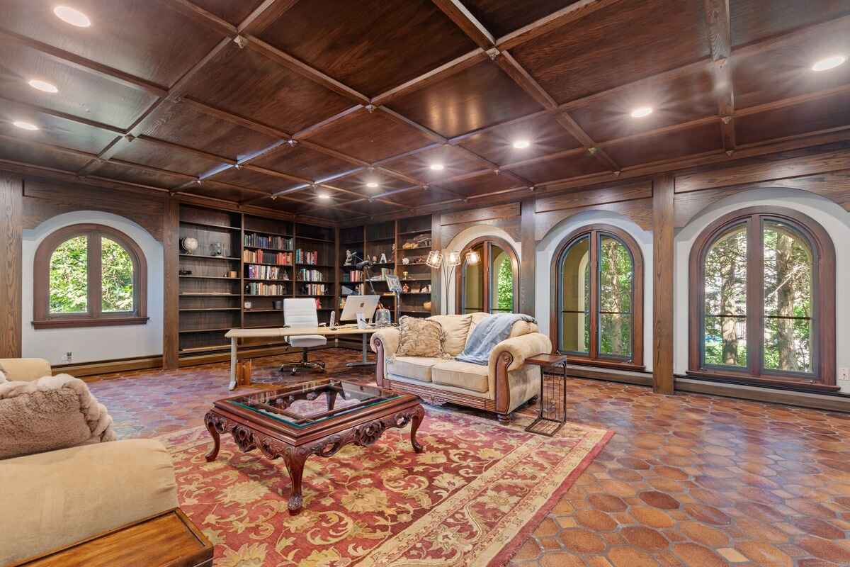 Library with a wood-paneled ceiling, arched windows, and a comfortable seating area.