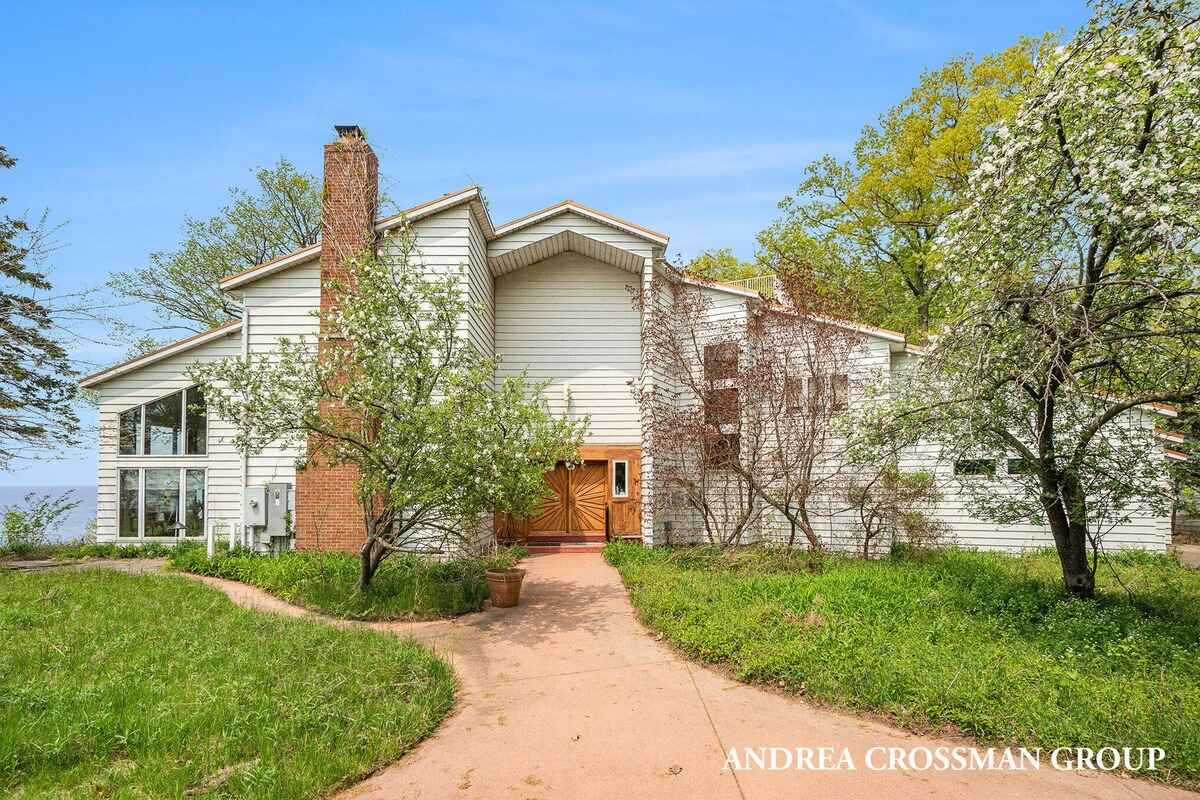 Large, white, single-family home with a brick chimney and wood front door sits on a grassy lot.