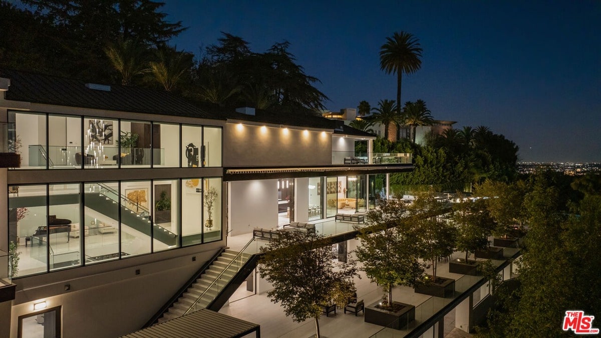 Perched majestically on a hillside, this architectural marvel boasts expansive glass walls that seamlessly blend indoor and outdoor living. The meticulously landscaped grounds, illuminated for nighttime splendor, complete the picture of sophisticated luxury.