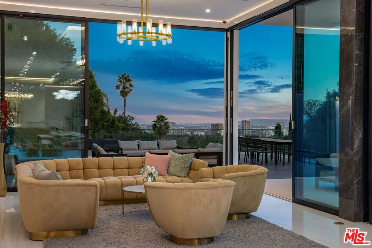 Floor-to-ceiling windows showcasing breathtaking city views are the undeniable centerpiece of this luxurious living room. The curved sectional sofa and elegant chandelier complement the panoramic vista, creating a sophisticated and inviting atmosphere perfect for relaxation and entertaining.