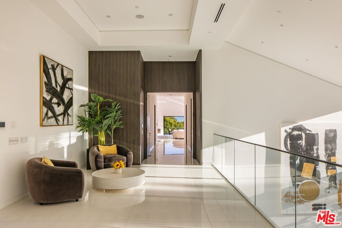 A dramatic interplay of light and shadow highlights the architectural details of this expansive hallway, creating a sense of both grandeur and intimacy. The carefully curated artwork and comfortable seating areas add a touch of personal style to the otherwise minimalist design.