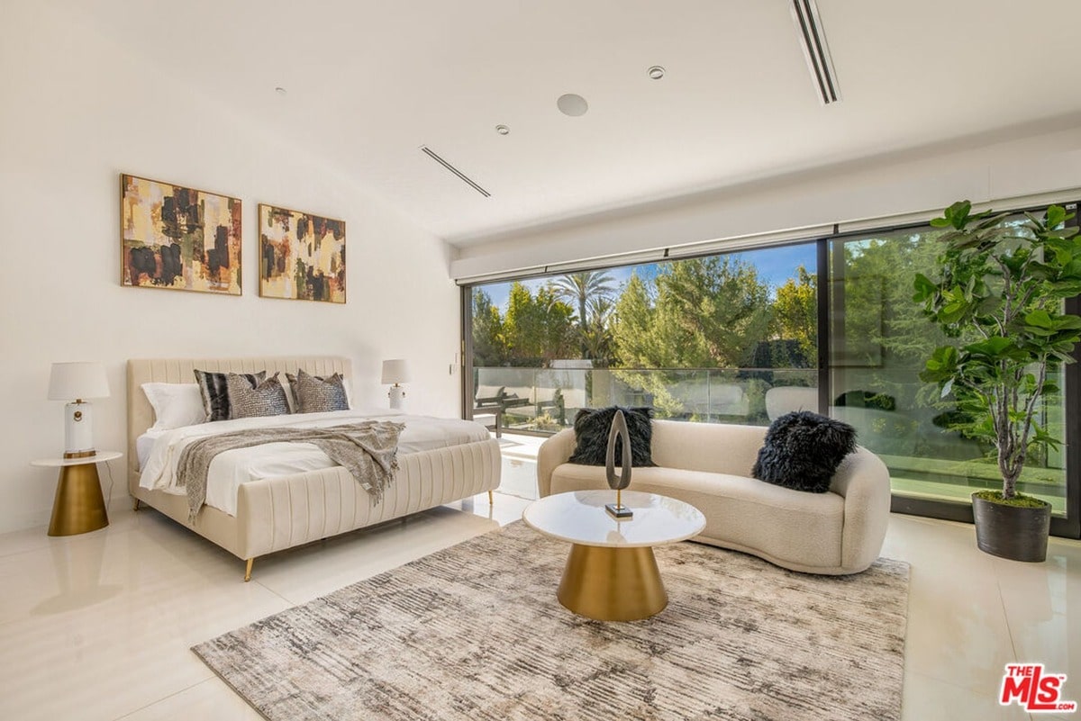 Natural light floods this expansive bedroom, highlighting the clean lines and neutral palette of the modern furnishings. Floor-to-ceiling windows offer a stunning view of the surrounding landscape, blurring the boundaries between indoor and outdoor spaces and creating a tranquil retreat.