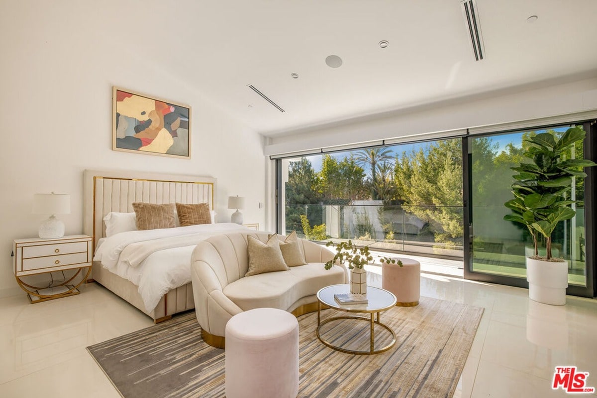 Natural light floods this expansive bedroom, highlighting the clean lines and neutral palette of the modern furnishings. Floor-to-ceiling windows offer a stunning view of the surrounding greenery, blurring the boundaries between indoor and outdoor spaces and creating a peaceful retreat.