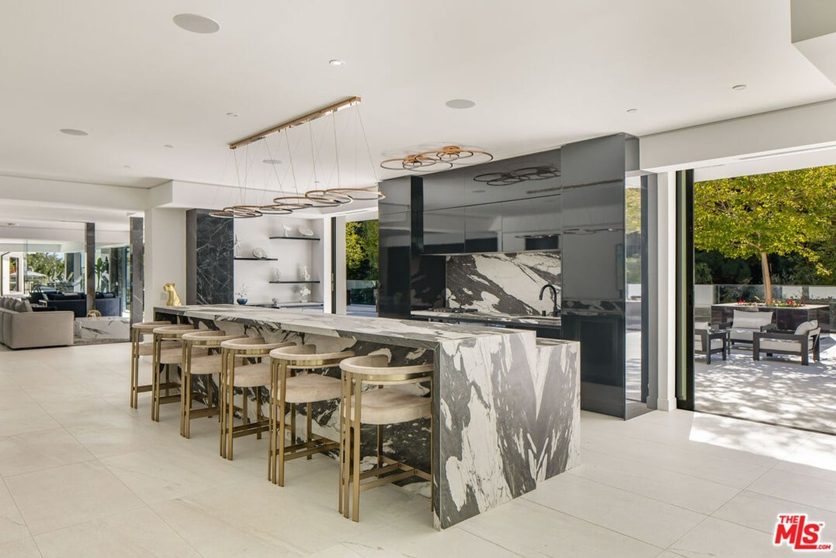 This expansive kitchen is a masterpiece of modern design, featuring a stunning marble island that serves as both a culinary workspace and a stylish gathering spot. Sleek cabinetry and a dramatic backsplash create a sophisticated atmosphere, while floor-to-ceiling windows offer a seamless transition to the outdoor patio.