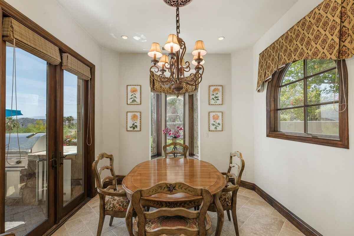 Dining nook with a wooden table, ornate chandelier, and windows offering outdoor views.