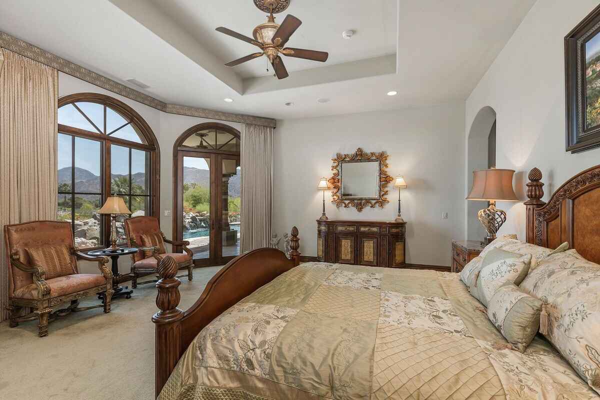 Master bedroom with arched windows, a seating area, and views of the pool and mountains.